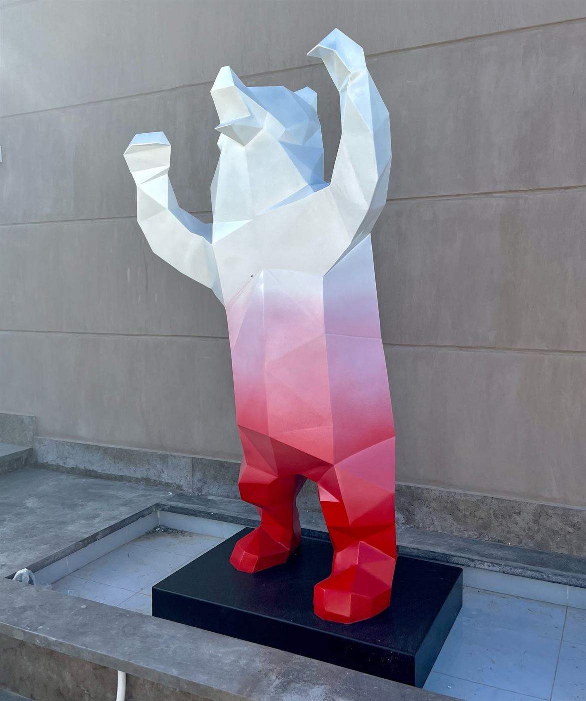 Faceted bear sculpture with raised arms, white fading to red