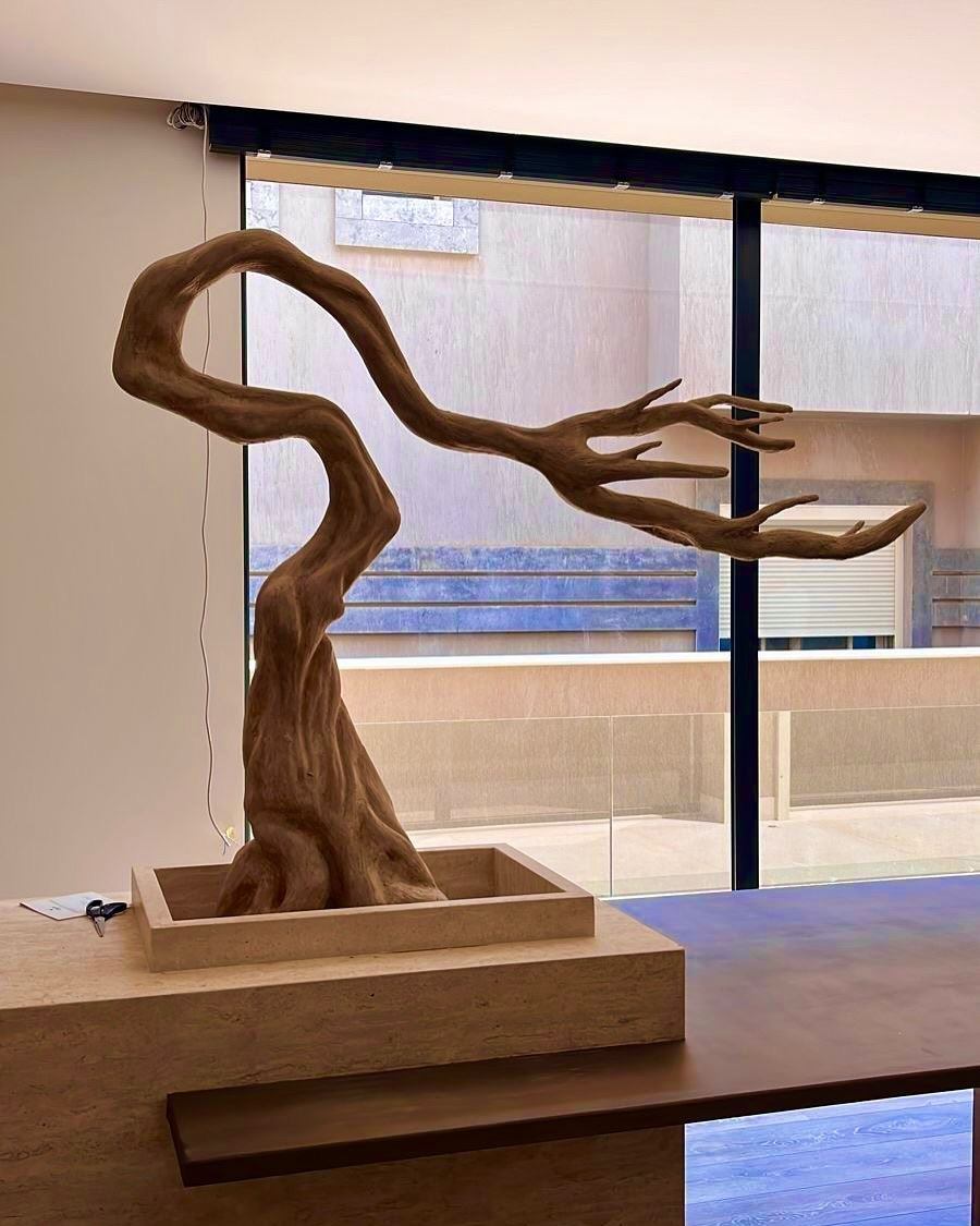 Sculpted windswept tree emerging from a stone table by a panoramic window