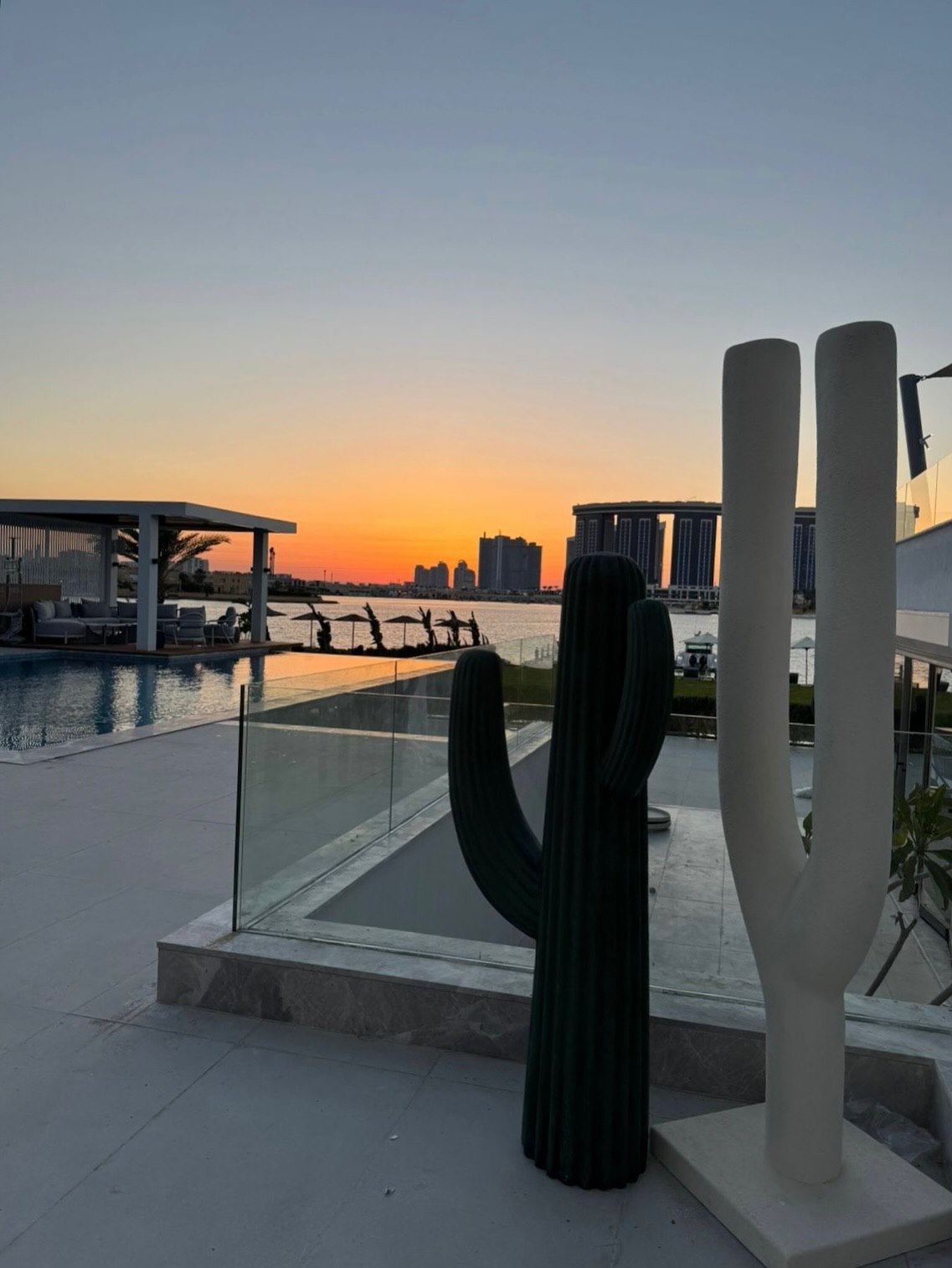 Two sculpted cacti on the same terrace against an orange sunset over the water