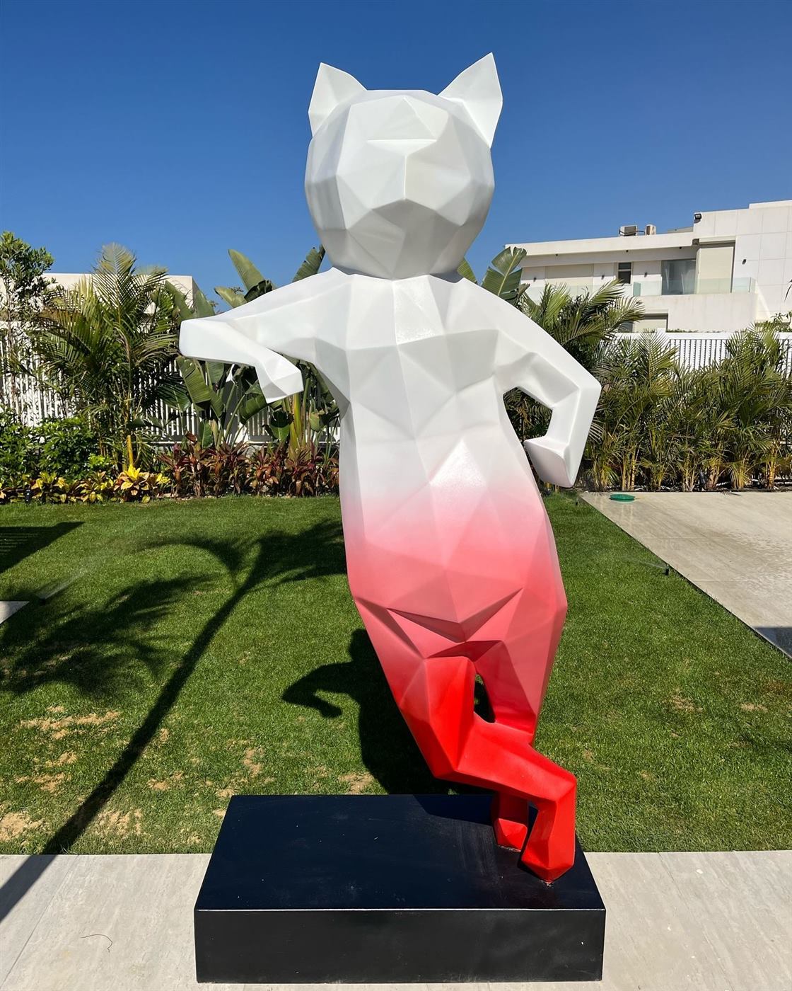 Faceted cat sculpture fading from white to red, leaning in a villa garden