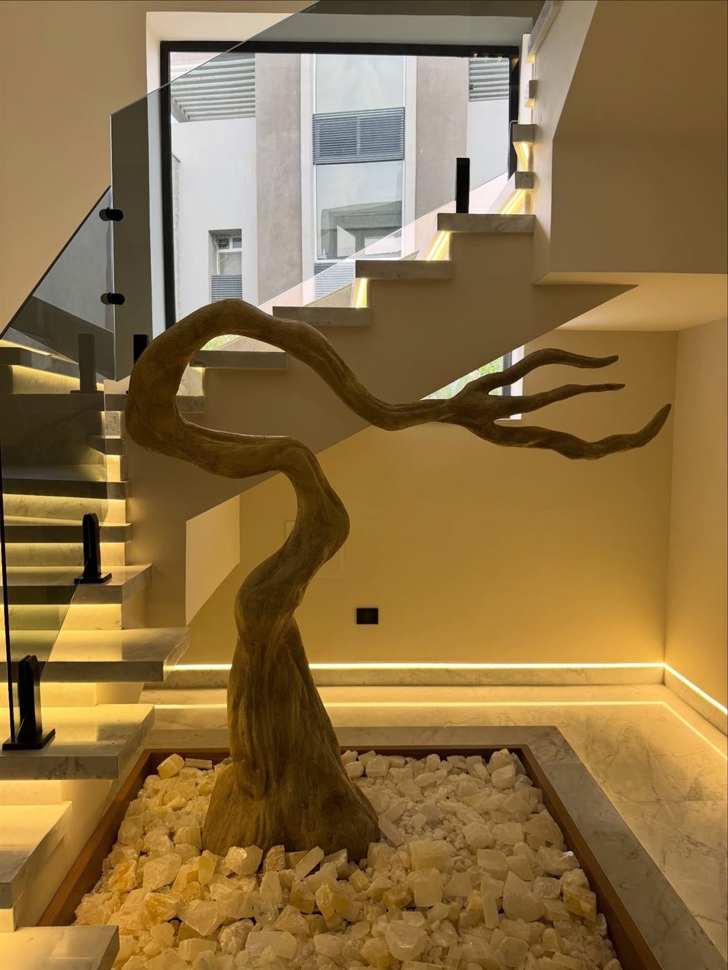 Gilded sculpted tree over a bed of pale stones under a staircase