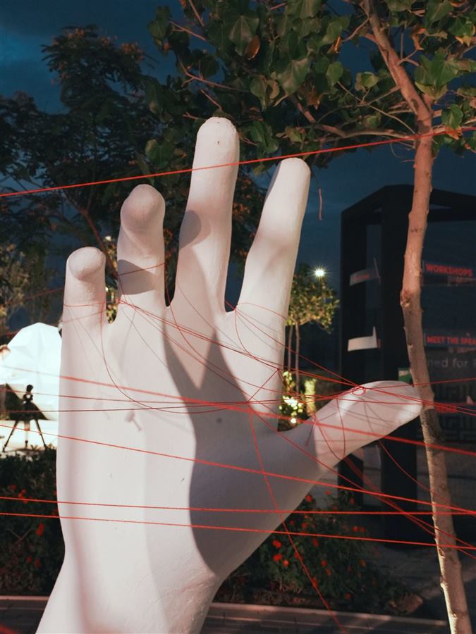 Giant white hand threaded with red strings at night