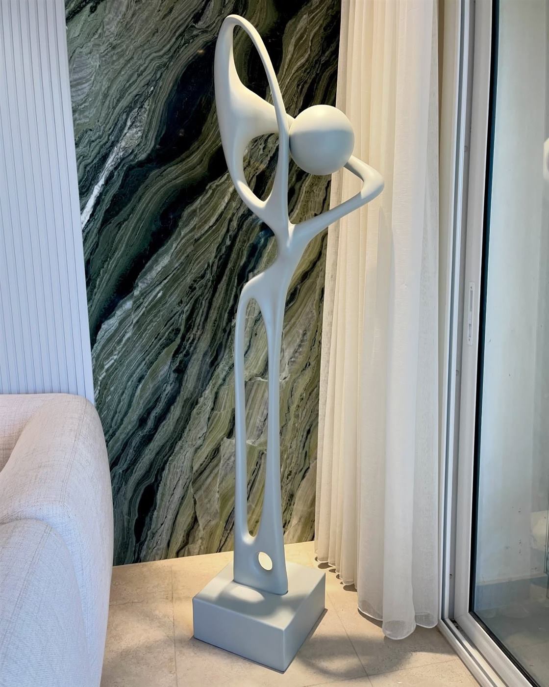 White abstract figure raising a sphere, standing by a marble wall