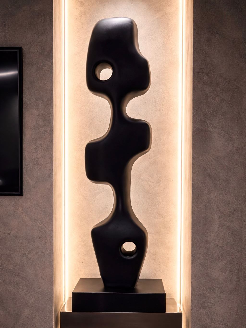 Black perforated totem sculpture lit inside a stone niche